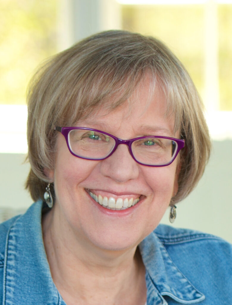 A photo of Martha Carlson, a white woman who is smiling and wearing eyeglasses and a denim jacket.